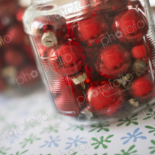 Red glass ball Christmas ornaments in glass jars on a tabletop.