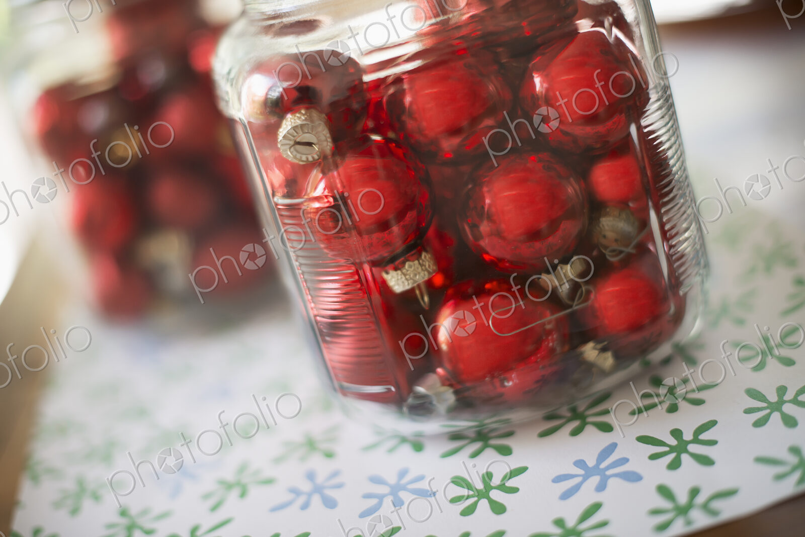 Red glass ball Christmas ornaments in glass jars on a tabletop.