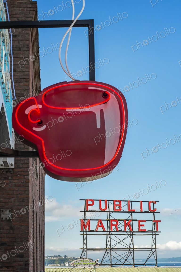 Red neon coffee cup sign glows beside the iconic Public Market sign at Pike Place…