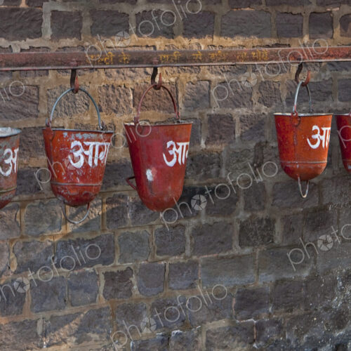Red sand fire buckets hanging from a railing on a brick wall in the station of the…