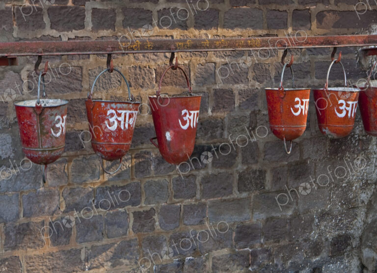 Red sand fire buckets hanging from a railing on a brick wall in the station of the…
