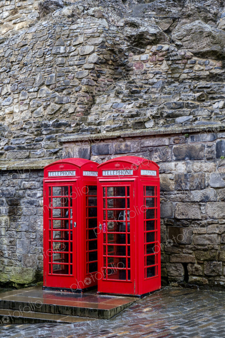 Red telephone boxes in front of ancient stone wall.