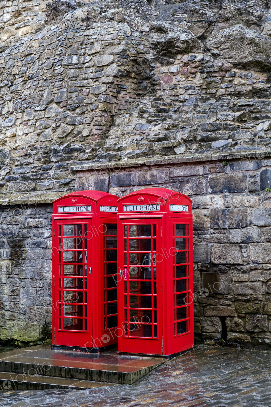 Red telephone boxes in front of ancient stone wall.