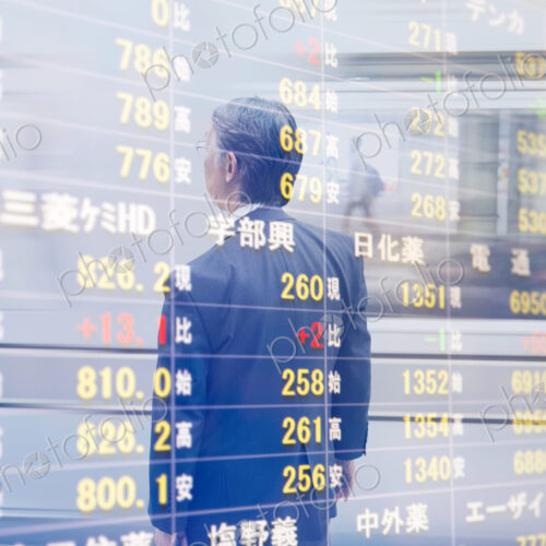 Reflection in glass of man in front of stock exchange information board.