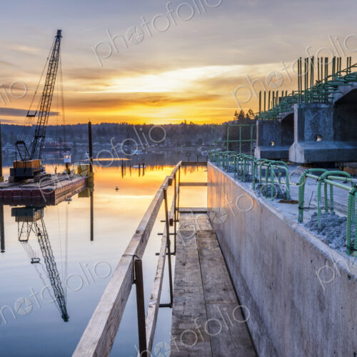 Reflection of bridge construction and sunset in still bay