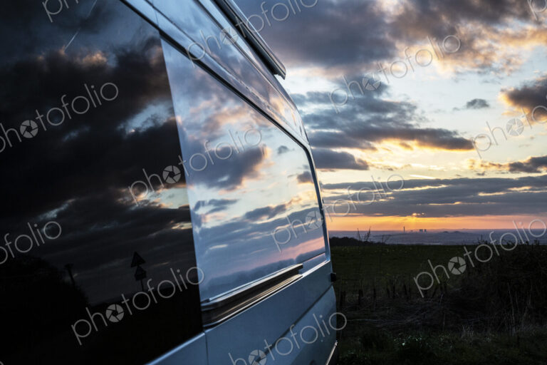 Reflections of clouds on camper van window at sunset.