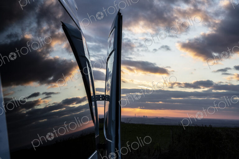 Reflections of clouds on camper van window at sunset.