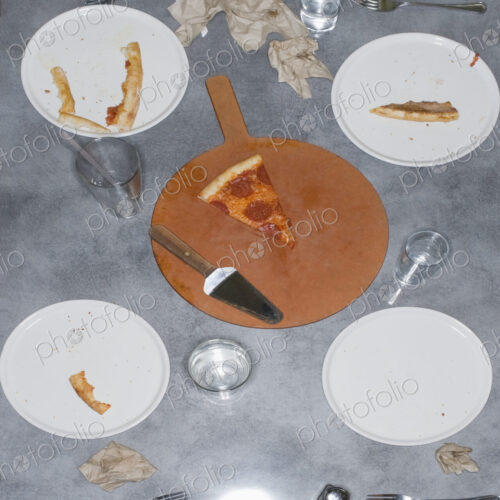 Remains of a pizza meal with leftover slice and crusts, glasses and plates and napkins.