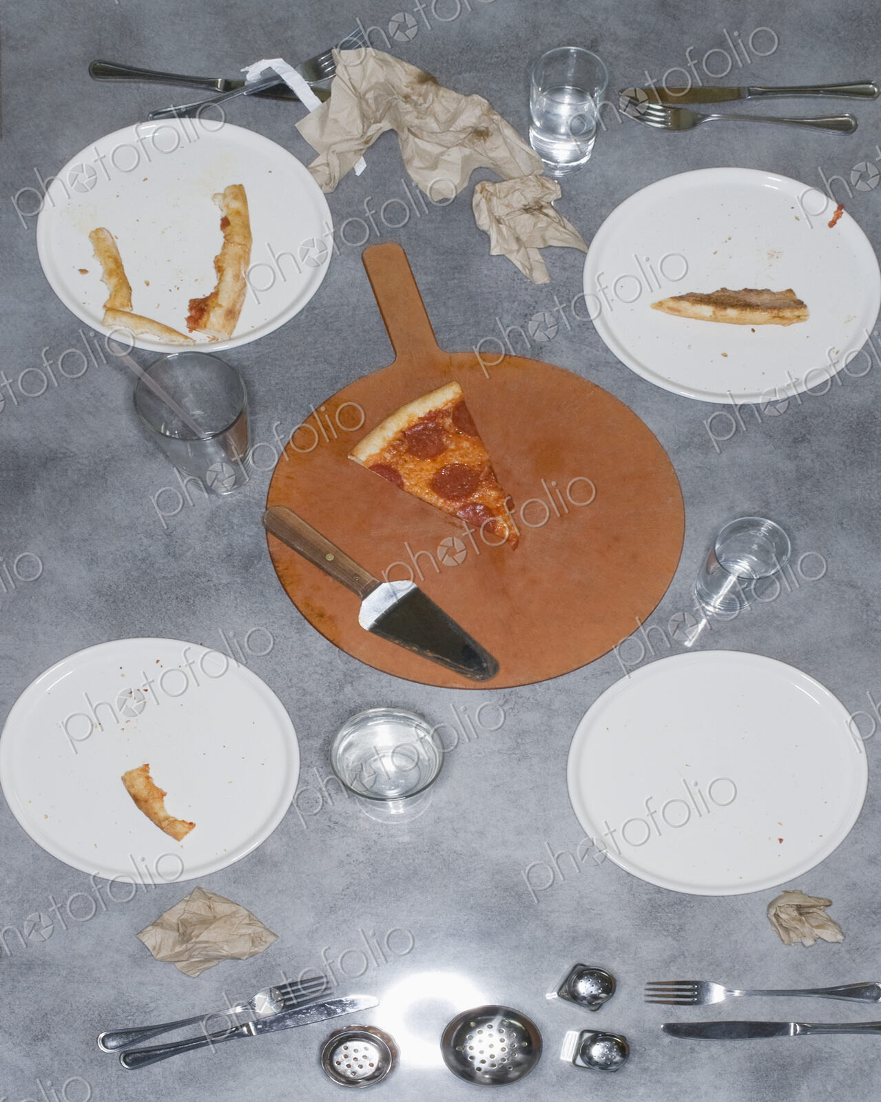 Remains of a pizza meal with leftover slice and crusts, glasses and plates and napkins.