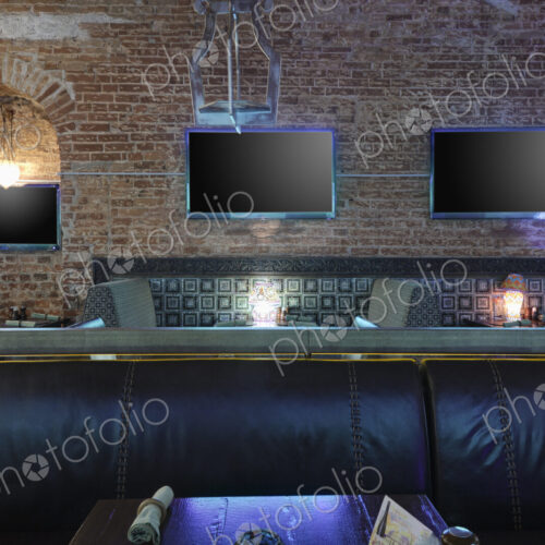 Restaurant tables with lamps under flat screen TVs.