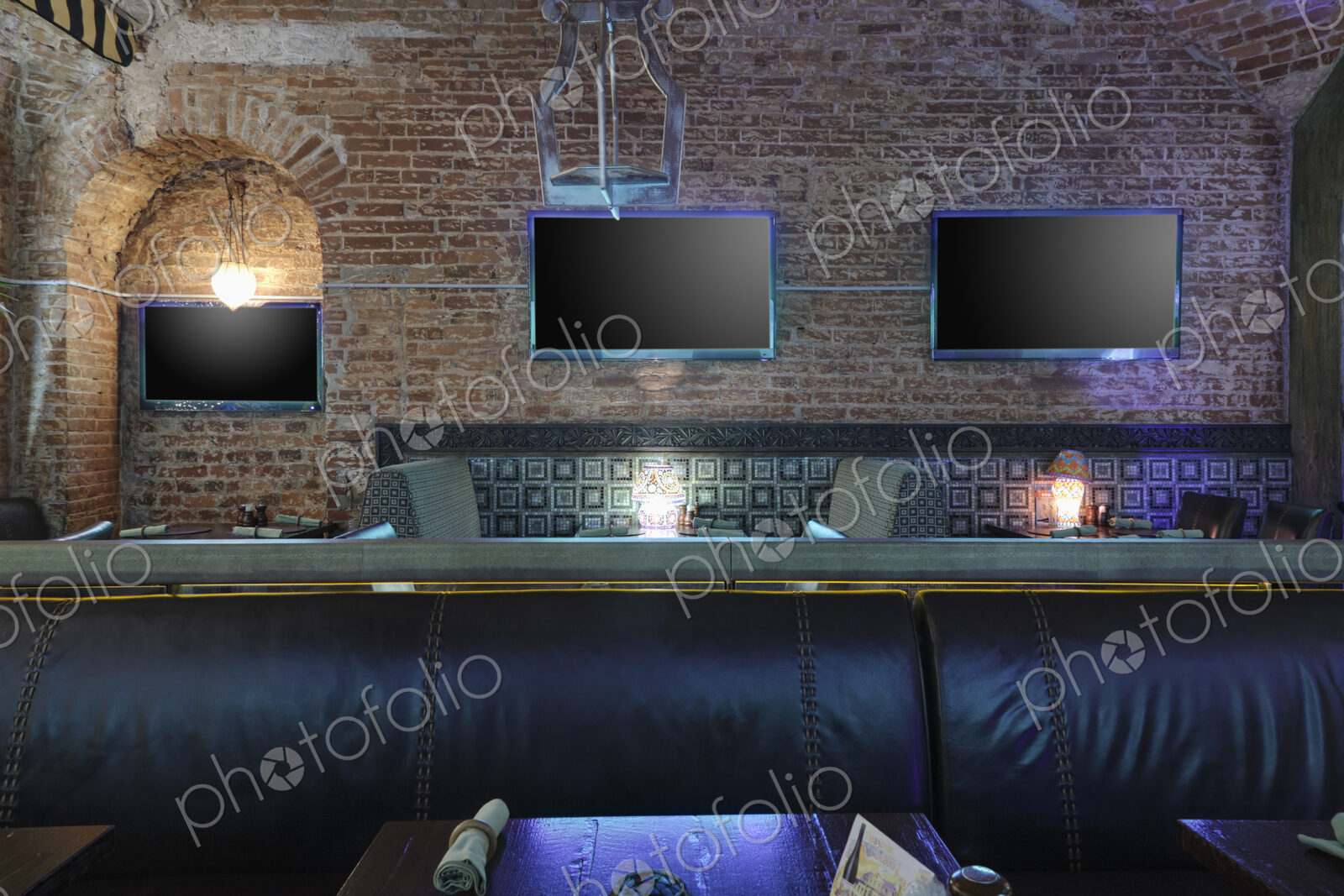 Restaurant tables with lamps under flat screen TVs.