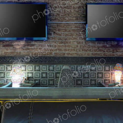 Restaurant tables with lamps under flat screen TVs.