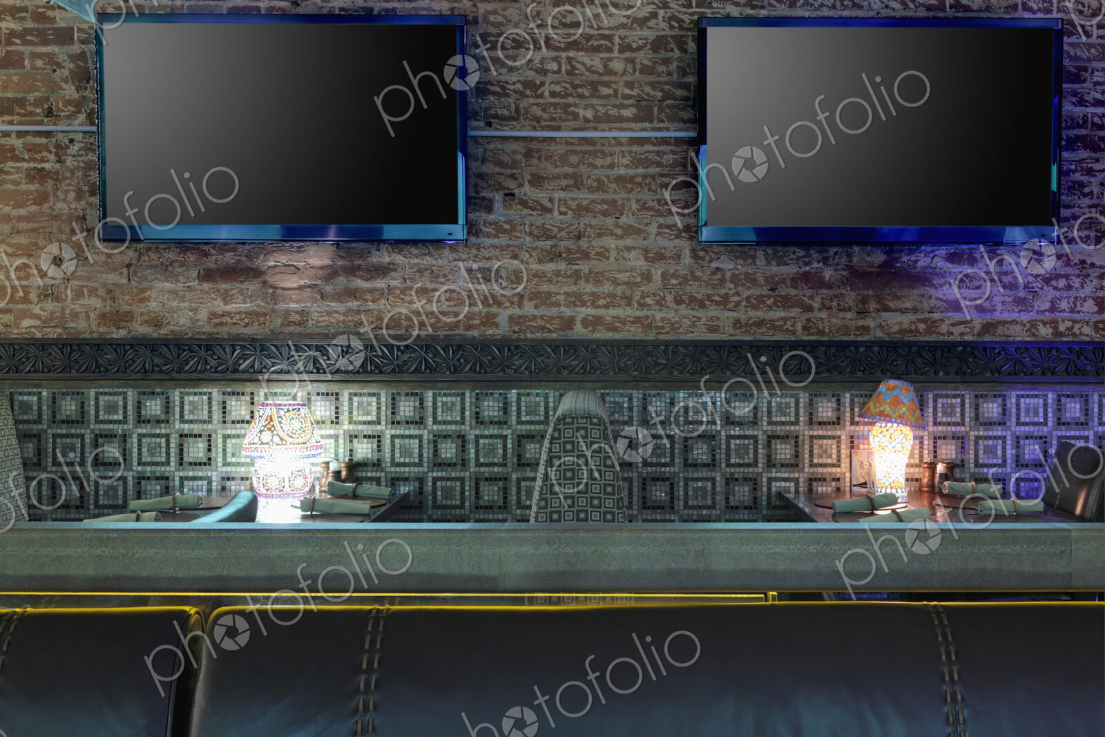 Restaurant tables with lamps under flat screen TVs.