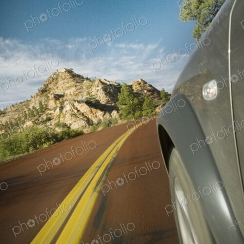 Road, a car travelling along, view of wheel arch and yellow road marking Road, a car travelling along, view of wheel arch and yellow road marking