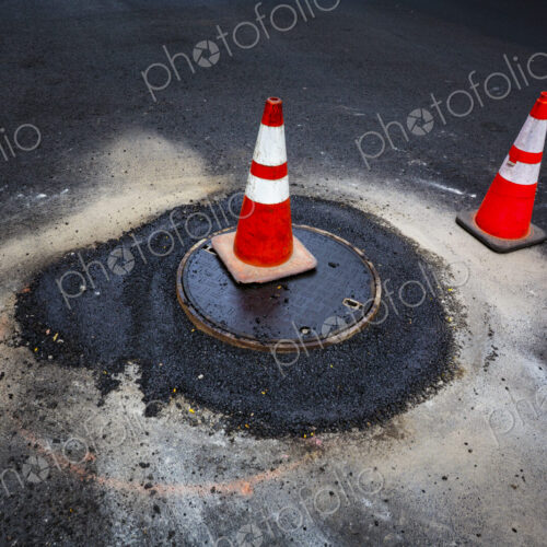 Road construction, a leak around a sewer manhole cover and traffic cones.