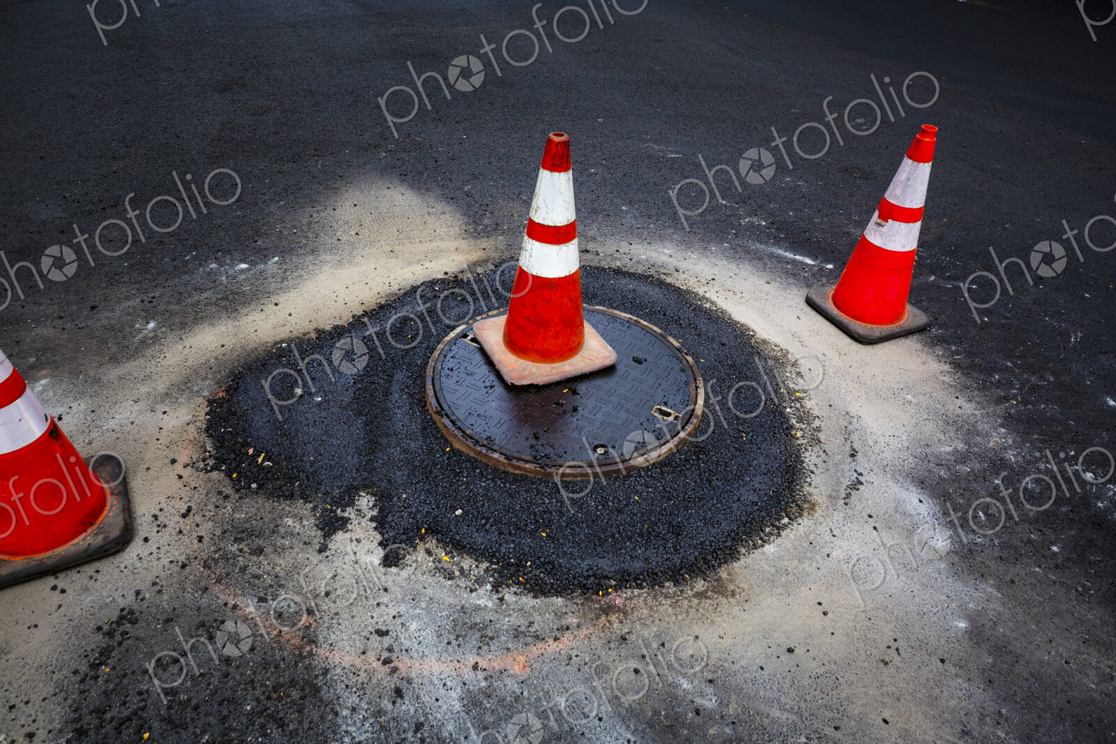 Road construction, a leak around a sewer manhole cover and traffic cones.