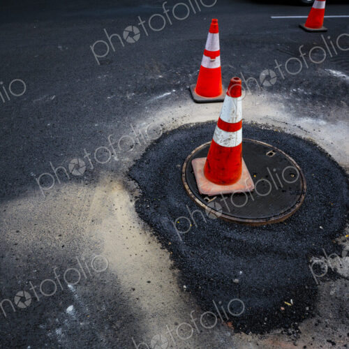 Road construction, flooding around a sewer manhole cover, traffic cones on the roadway.