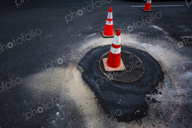 Road construction, flooding around a sewer manhole cover, traffic cones on the roadway.