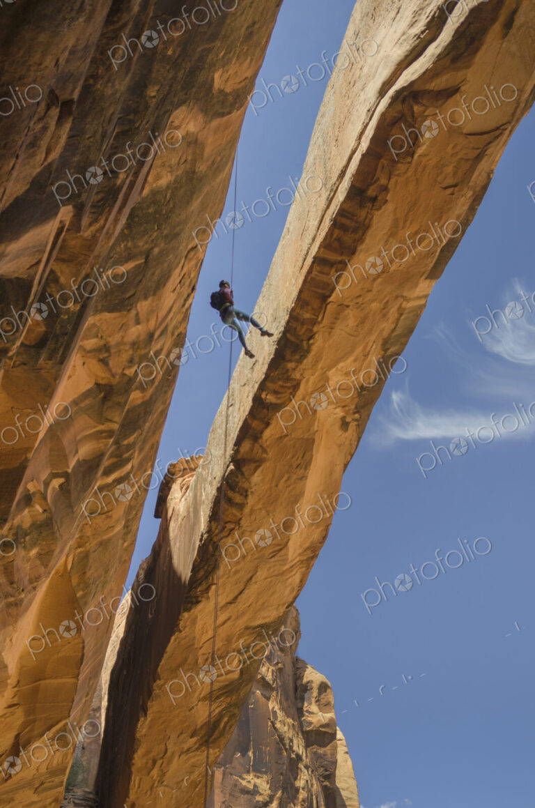 Rock climber hanging on rope on arch