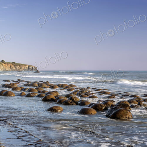 Rocks in shallow waves on Pacific Ocean at dusk.