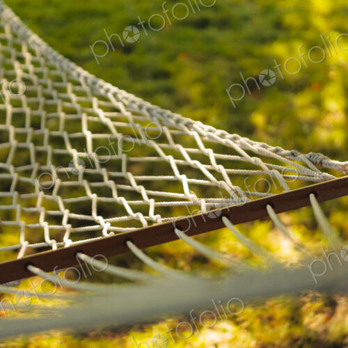 Rope hammock in the shade under a tree in a garden.