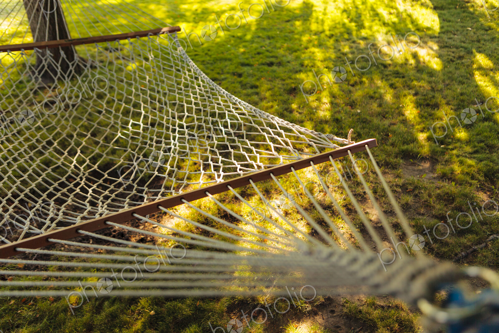Rope hammock in the shade under a tree in a garden.