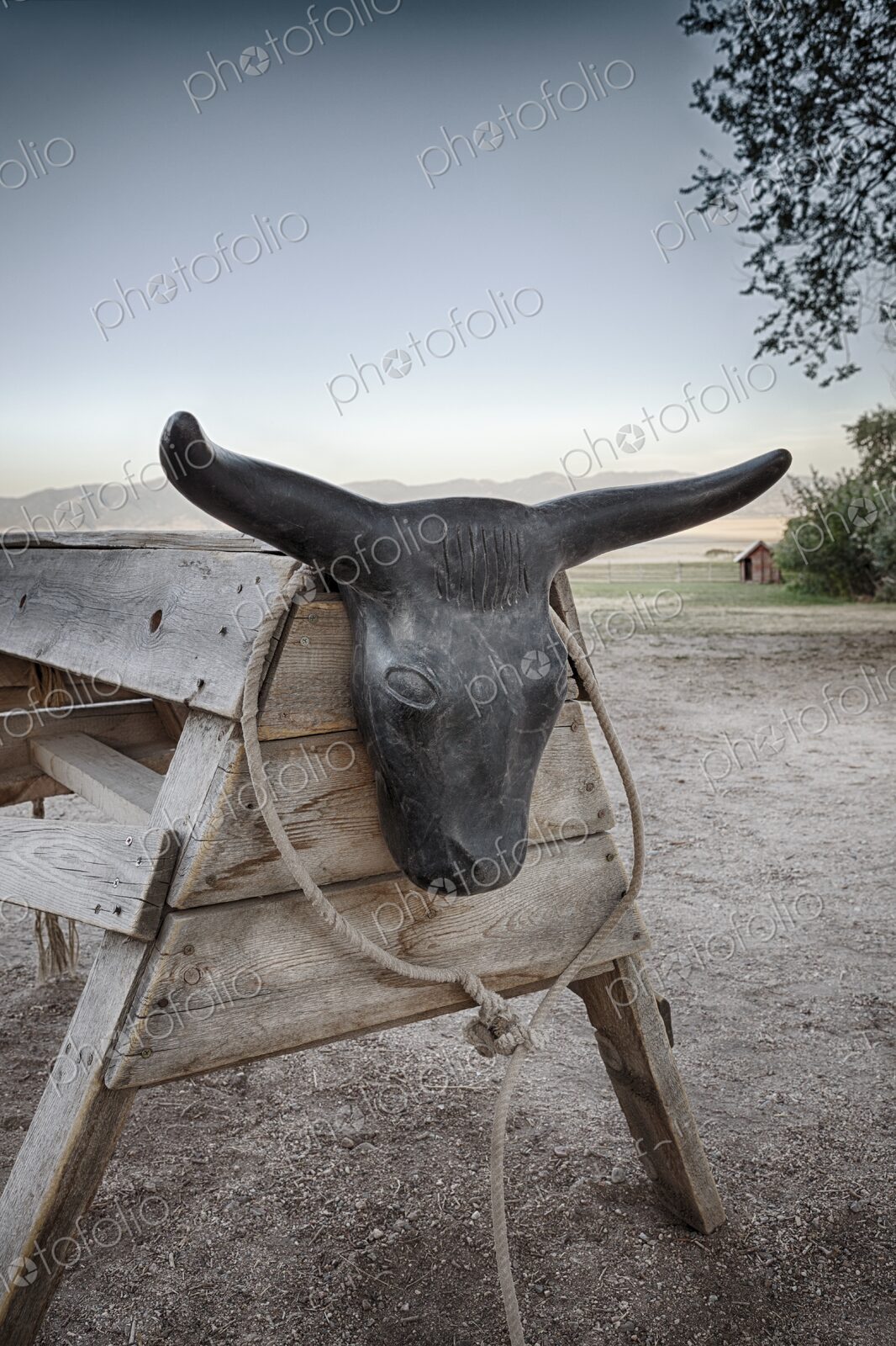 Roping dummy set up on dirt ranch ground, with coiled rope and mountain landscape in…