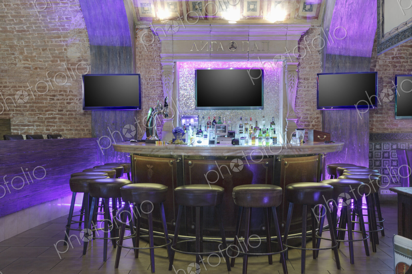 Round bar stand against three TV screens on brick wall.