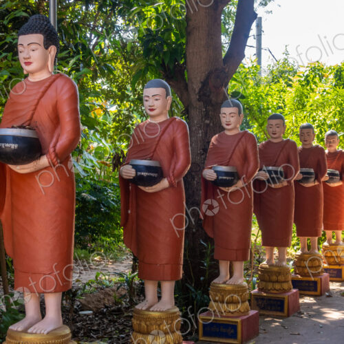 Row of Buddhist monk statues with red robes and alms bowls in the gardens of the… Row of Buddhist monk statues with red robes and alms bowls in the gardens of the…