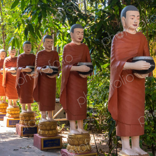 Row of Buddhist monk statues with red robes and alms bowls in the gardens of the… Row of Buddhist monk statues with red robes and alms bowls in the gardens of the…