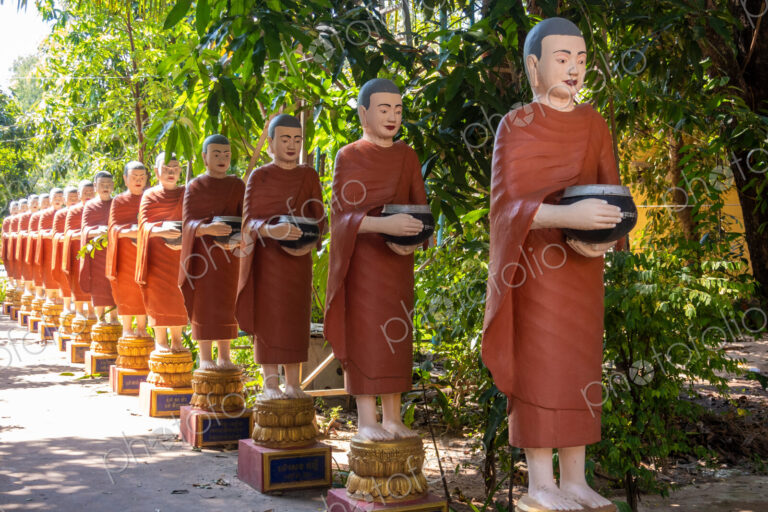 Row of Buddhist monk statues with red robes and alms bowls in the gardens of the…
