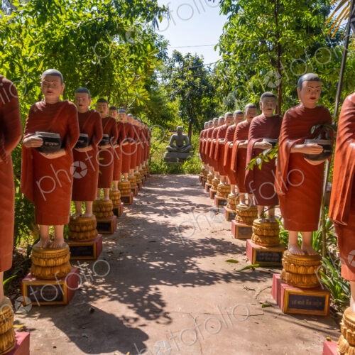 Row of Buddhist monk statues with red robes and alms bowls in the gardens of the… Row of Buddhist monk statues with red robes and alms bowls in the gardens of the…