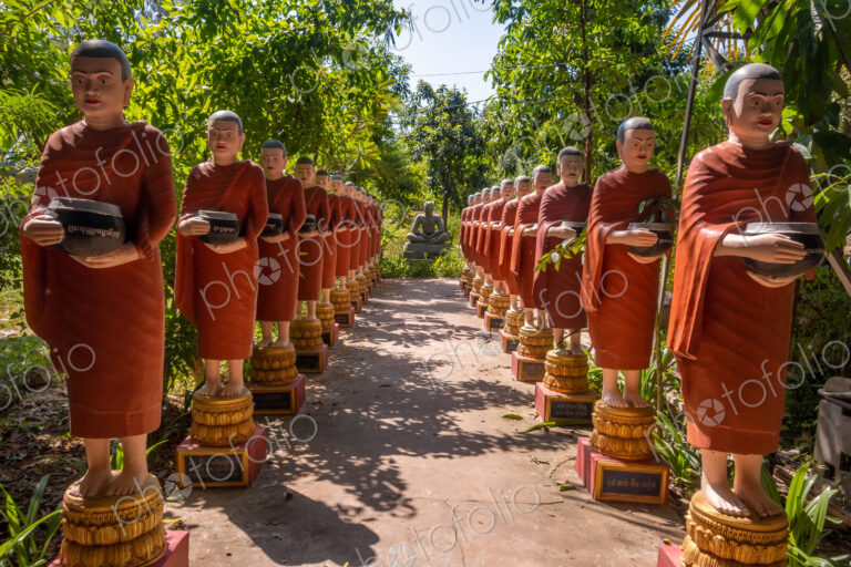 Row of Buddhist monk statues with red robes and alms bowls in the gardens of the…