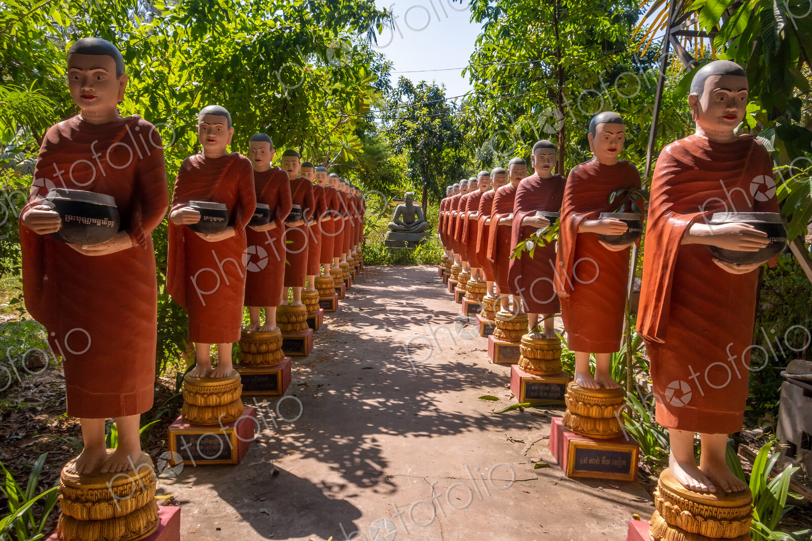 Row of Buddhist monk statues with red robes and alms bowls in the gardens of the…