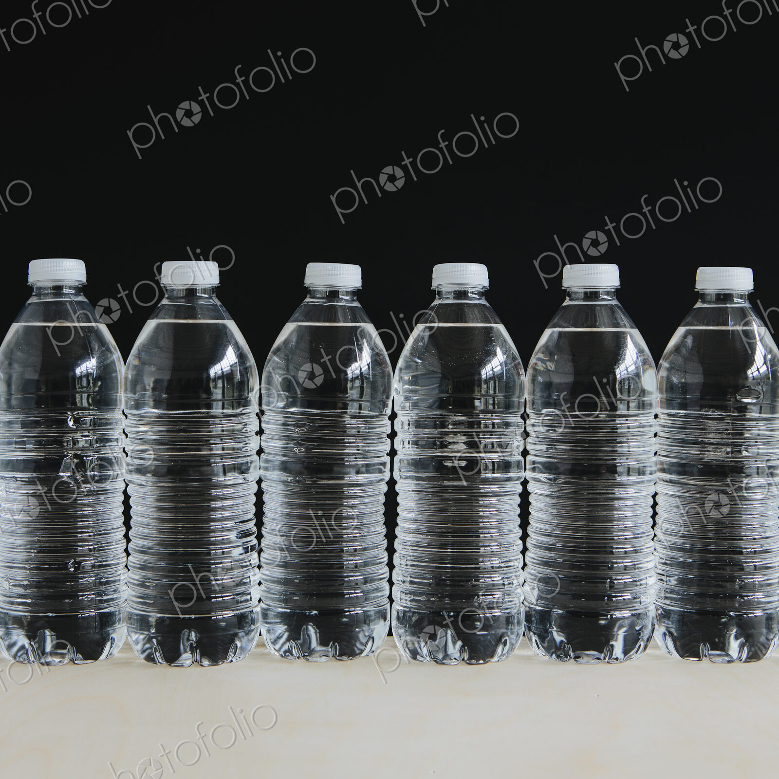 Row of clear, plastic water bottles filled with filtered water in a row, on a black…
