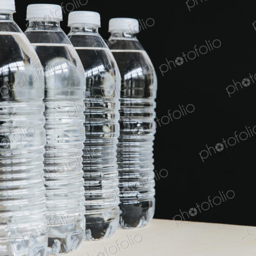 Row of clear, plastic water bottles filled with filtered water in a row. on a black…