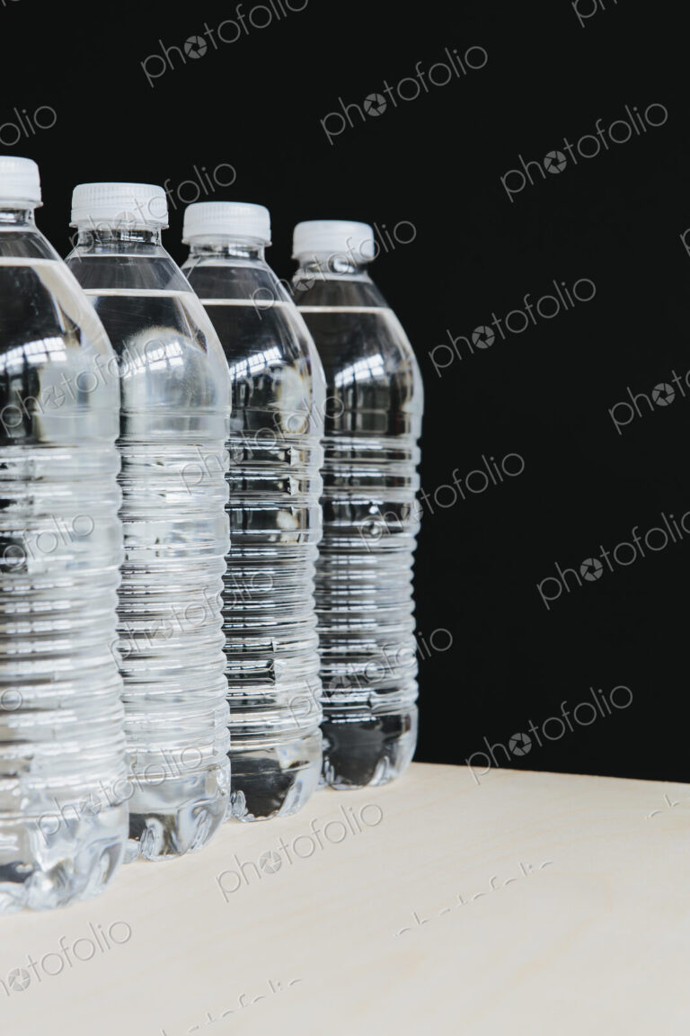Row of clear, plastic water bottles filled with filtered water in a row. on a black…