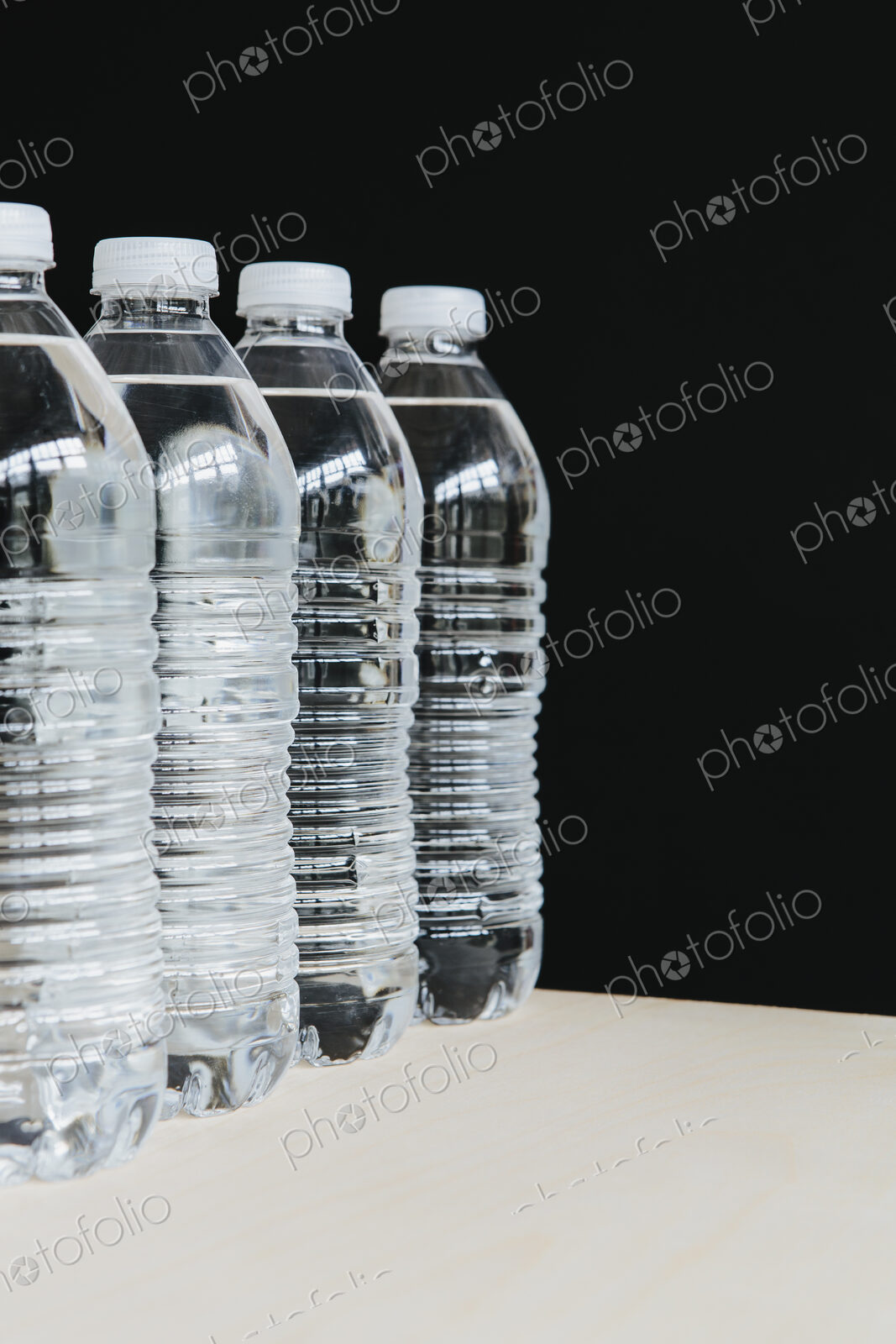 Row of clear, plastic water bottles filled with filtered water in a row. on a black…