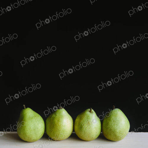 Row of four green Anjou pears, black background