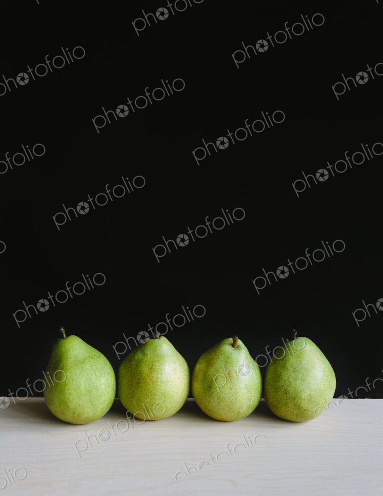 Row of four green Anjou pears, black background