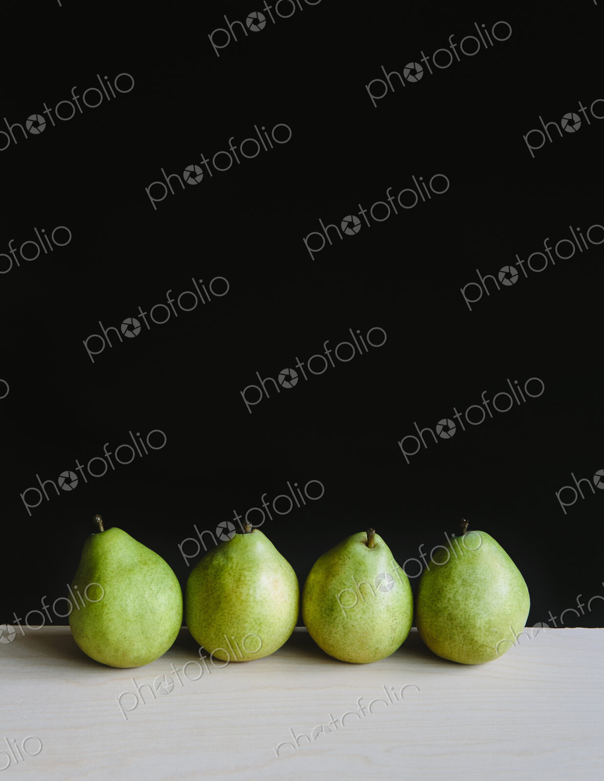 Row of four green Anjou pears, black background