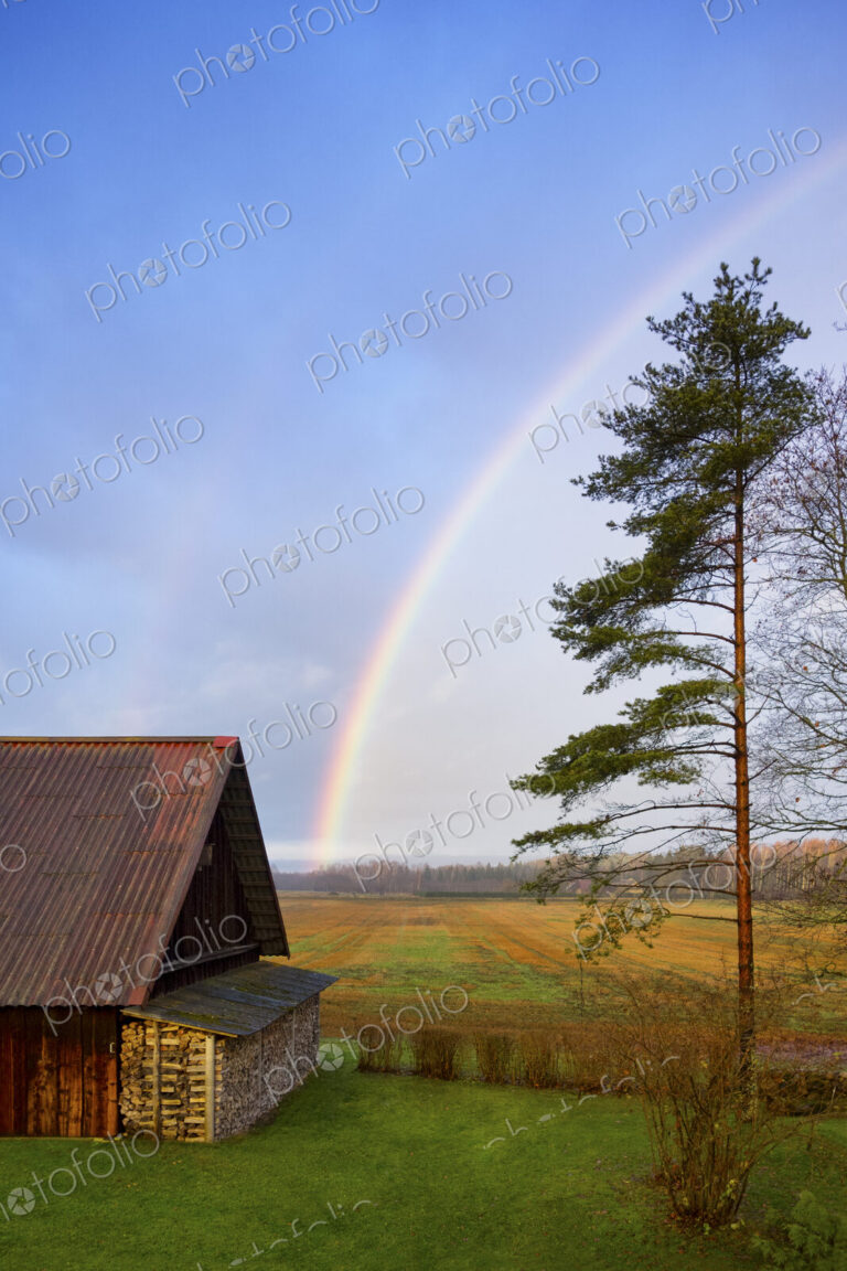 Rural scene, a rainbow in the sky over a barn, after rain.