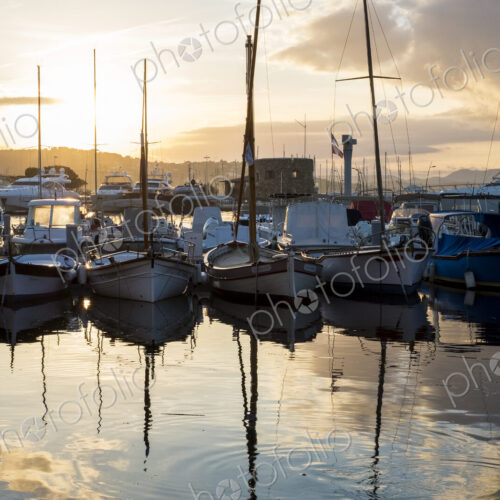 Sailboats moored in harbour reflected in calm sea at sunset. Sailboats moored in harbour reflected in calm sea at sunset.
