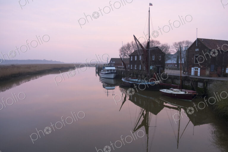Sailing boats moored at harbour wall, reflected on the surface of a calm canal at…