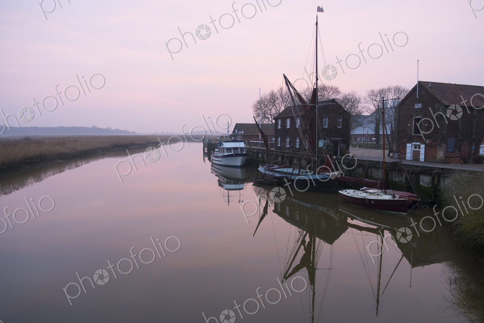 Sailing boats moored at harbour wall, reflected on the surface of a calm canal at…
