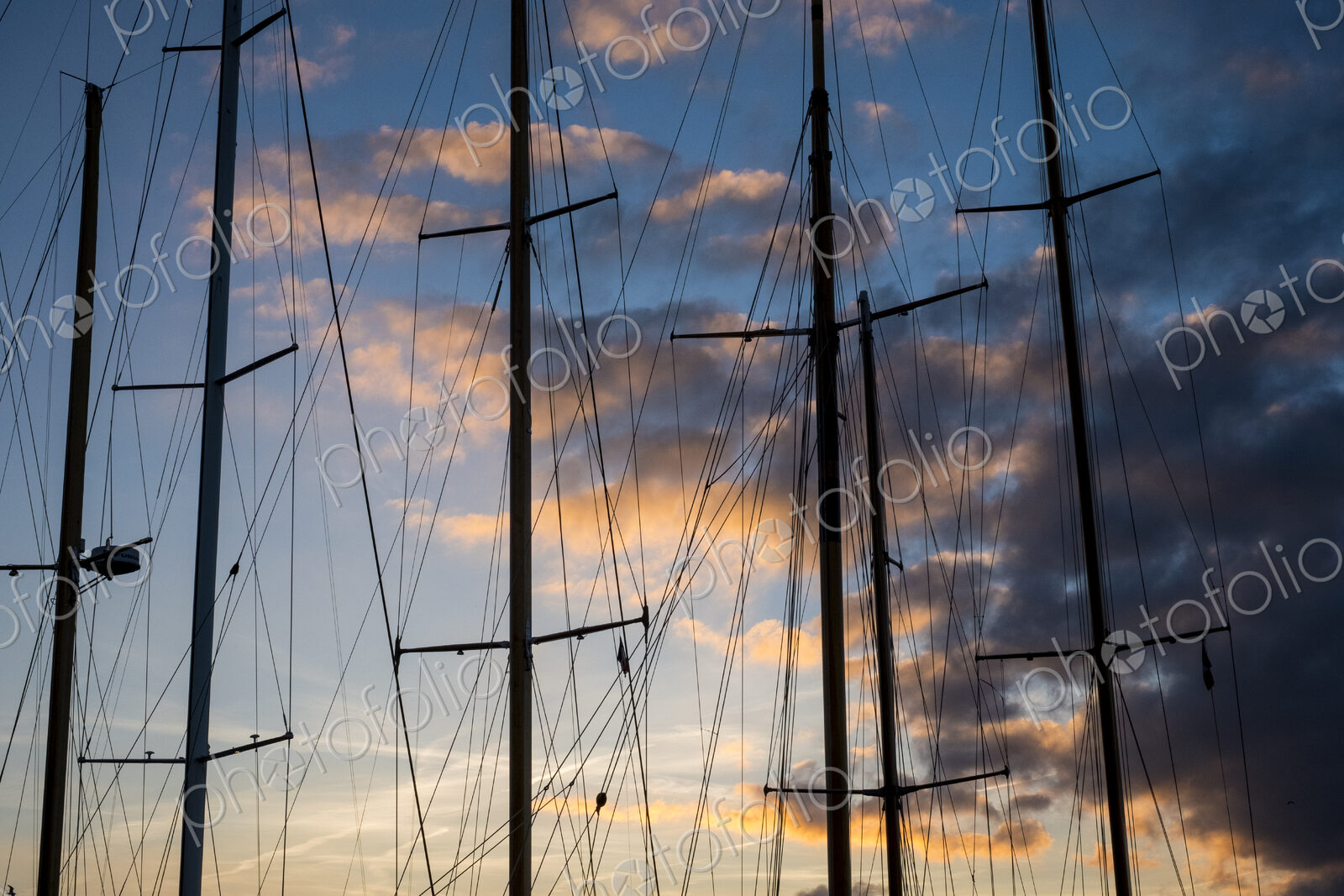 Sailing ship masts and rigging against a cloudy sky at sunset.