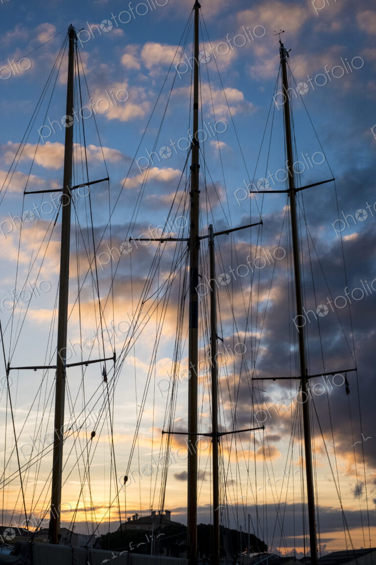 Sailing ship masts and rigging against a cloudy sky at sunset.