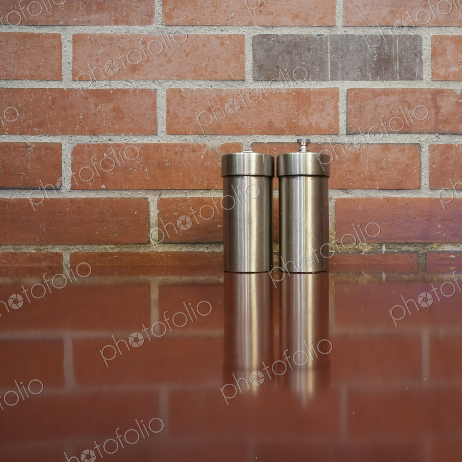 Salt and pepper shakers on table with brick wall behind.