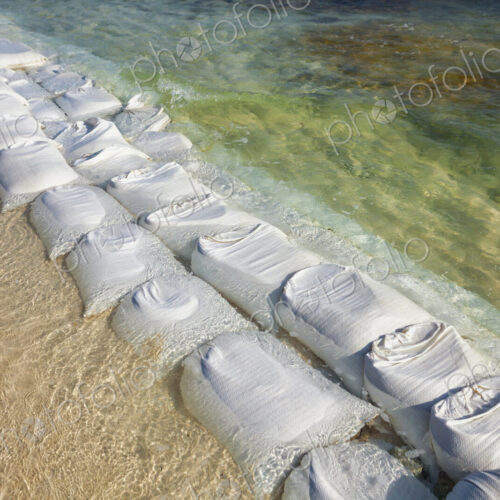 Sandbags in rows at the water's edge to prevent erosion of the beach