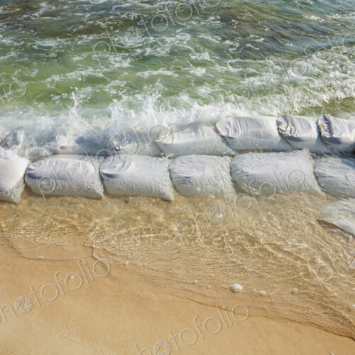 Sandbags in rows at the water's edge to prevent erosion of the beach